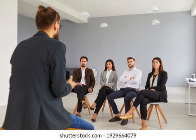 Young Personal Growth Coach Talking To Group Of Young People In Modern Workspace. Serious Students, Entrepreneurs Or Office Workers Listening To Male Business Trainer Who Sharing Life Experience