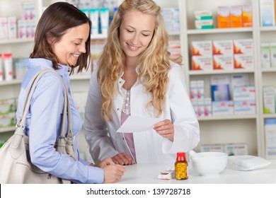 Young Pharmacist And Female Customer Reading Prescription Paper At Pharmacy Counter