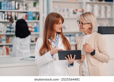 Young pharmacist is showing a digital tablet to a senior customer while they're discussing about medication in a pharmacy - Powered by Shutterstock