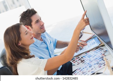 Young photo editors pointing at a computer screen while working on contact sheets - Powered by Shutterstock