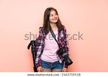 Young photographer girl over isolated pink background laughing and looking up