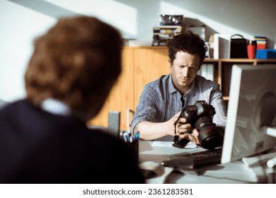 Young photographer going through his camera at his desk office - Powered by Shutterstock