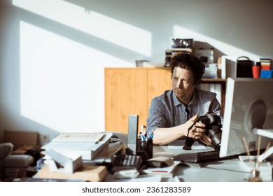 Young photographer going through his camera at his desk office - Powered by Shutterstock