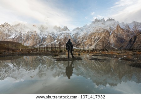 Young photographer looking at Passu Cathedral mountain in Pakistan and reflection on the water. Mountain landscape with reflection on the water