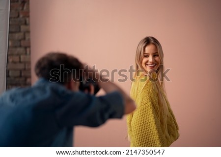 Young photographer taking picures of model, backstage of photoshooting in studio.