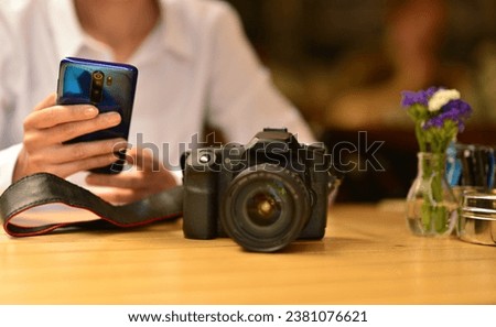 Young photographer woman sitting at the table in the cafe and monitoring work on the phone