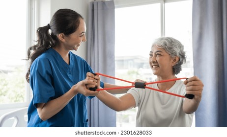 Young physical therapist caregiver assisting mature asian woman grey hair doing exercise with elastic bands at physiotherapy clinic. - Powered by Shutterstock