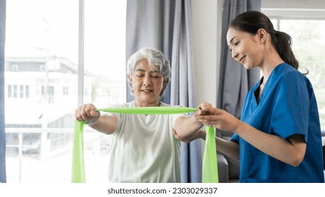 Young physical therapist caregiver assisting mature asian woman grey hair doing exercise with elastic bands at physiotherapy clinic. - Powered by Shutterstock