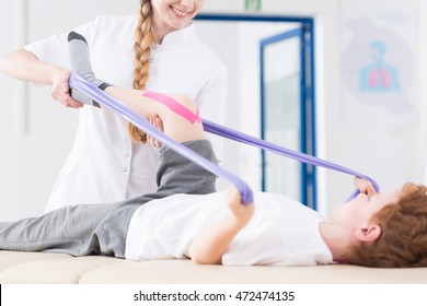 Young physiotherapist and boy exercising with resistance band, having kinesio tape on his knee