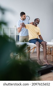 Young Physiotherapist Examining Middle Aged African American Man On Blurred Foreground