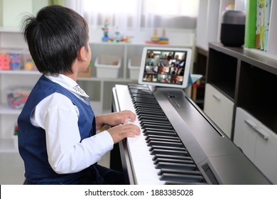 Young pianist boy looking at the digital tablet screen for learning piano online at home. Music distance learning concept.