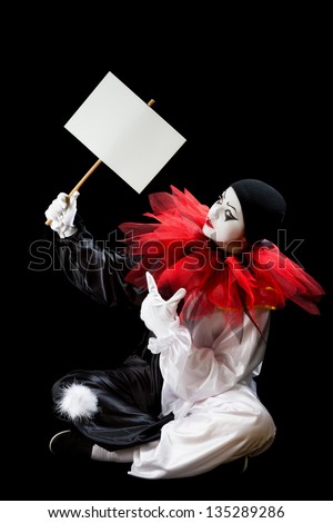 Young Pierrot sitting on a black background holding an empty sign