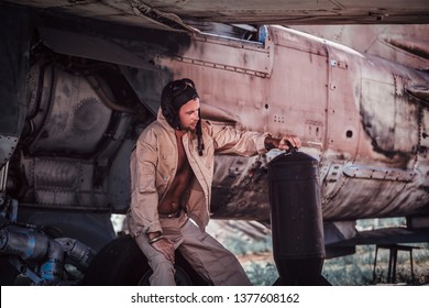 Young Pilot Is Woking Hard. It's Hot Summer Outside. Behide The Pilot Is Aircraft. Pilot Hold In His Hands Bottle Of Gasoline.