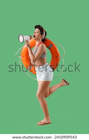 Young pin-up lifeguard with ring buoy shouting into megaphone on green background