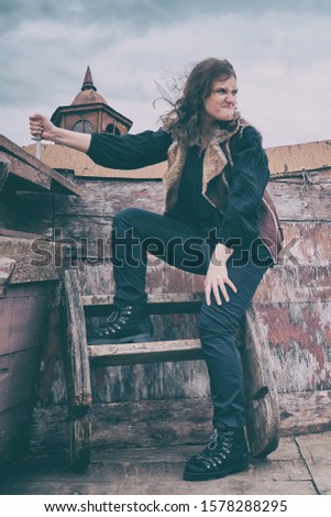 A young pirate woman with an evil expression on the deck of an old ship. Angry girl robber with a knife in his hand