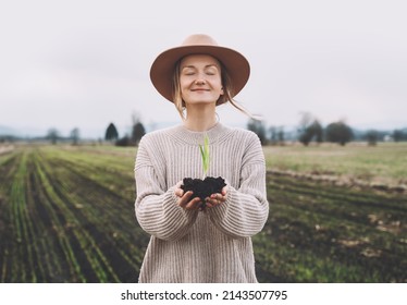 Young plant in hands in background of agricultural field area. Woman holding in hands green sprout seedling on black soil. Concept of Earth day, organic gardening, ecology, sustainable life. - Shutterstock ID 2143507795