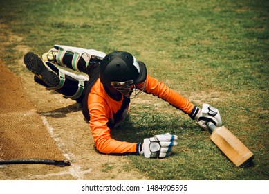 Young Player Fallen On The Ground Holding A Cricket Bat In Hand