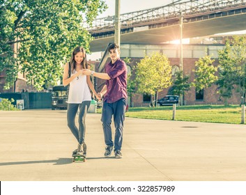 Young playful couple having a romantic date outdoors - Sportive man teaching her girlfriend to skateboarding - Teen lovers spending time together and having fun - Powered by Shutterstock