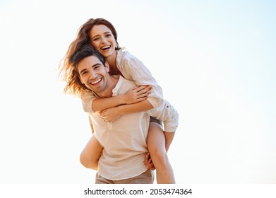Young playful fun happy enamored smiling couple two friends family man woman in casual clothes boyfriend give piggyback ride to joyful girlfriend sit on back look aside on light white sky background