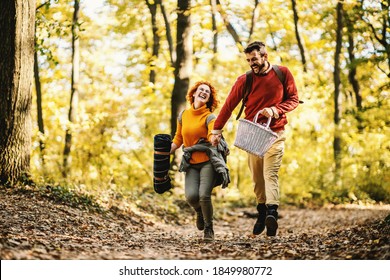 Young playful smiling happy couple in love holding hands and running in nature on a beautiful autumn day. Couple is holding picnic equipment.