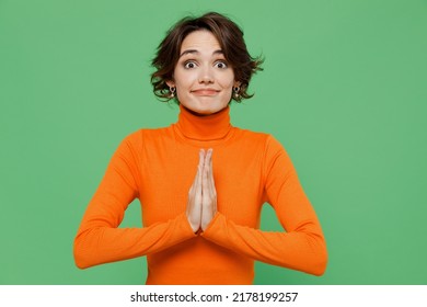 Young Pleaded Woman 20s In Orange Turtleneck Hold Hands Folded In Prayer Gesture, Begging About Something Isolated On Plain Pastel Light Green Color Background Studio Portrait People Lifestyle Concept