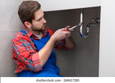 Young plumber is repairing a sink at the bathroom
