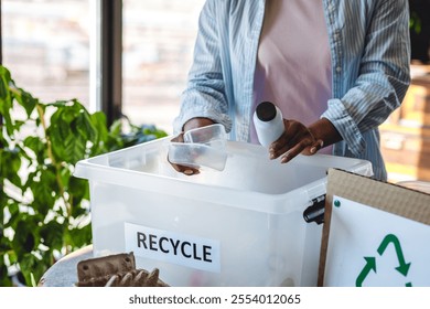 Young plus size African American woman doing waste sorting at home, care about planet, ecology. Containers for recyclable waste: plastic, glass, paper. Symbol of recycling, environment protect - Powered by Shutterstock