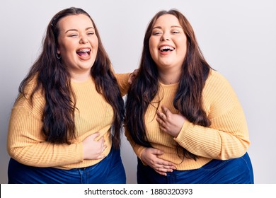 Young plus size twins wearing casual clothes smiling and laughing hard out loud because funny crazy joke with hands on body. 