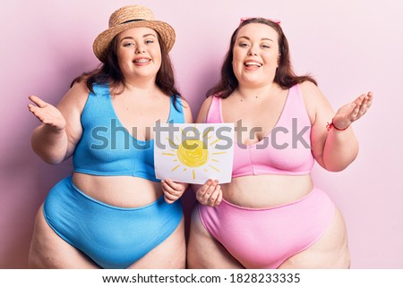 Young plus size twins wearing bikini holding sun draw celebrating achievement with happy smile and winner expression with raised hand 