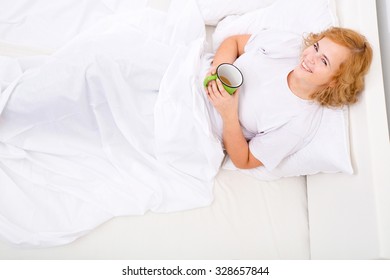 A young plus size woman drinking the first coffee of the day in bed.
 - Powered by Shutterstock