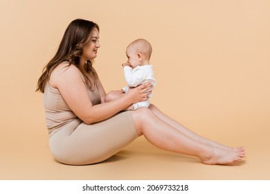 Young Plus Size Woman Holding Kid While Sitting On Beige Background