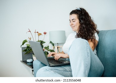 Young plus size woman smiling while working from home on his laptop on the sofa. Young entrepeneur freelancer. Remote tasking work, happy attitude, new job. Modern and young style. - Powered by Shutterstock