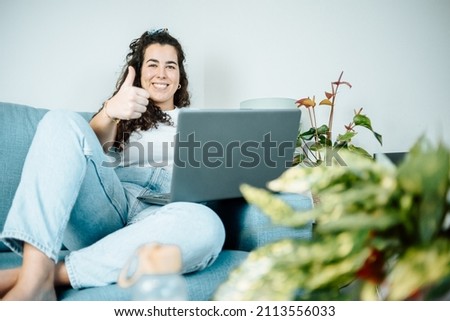 Young plus size woman smiling while working from home on his laptop on the sofa. Young entrepeneur freelancer. Remote tasking work, happy attitude, new job. Modern and young style.