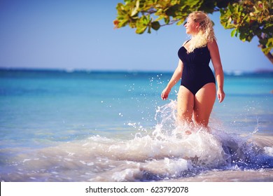 young plus size woman in swimwear enjoying vacation in water splash on the beach