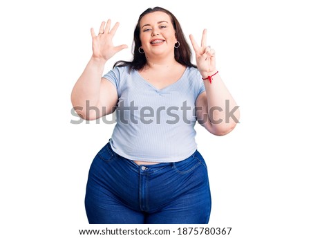 Young plus size woman wearing casual clothes showing and pointing up with fingers number seven while smiling confident and happy. 