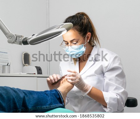 Young podiatrist doing chiropody in her podiatry clinic. The chiropodist is cutting the patient's nails with specialized scissors