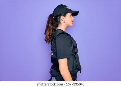 Young police woman wearing security bulletproof vest uniform over purple background looking to side, relax profile pose with natural face and confident smile.