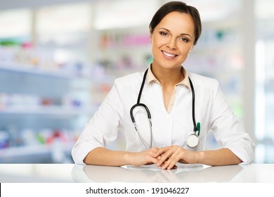 Young Positive Brunette Doctor Woman Behind Table In Drug Store 