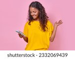 Young positive casual Indian woman teen rejoices in purchase of new phone and looks at gadget of flagship model with smile experiencing positive emotions from device stands on pink background.