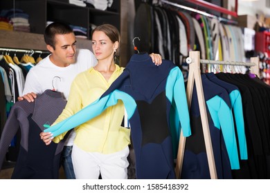 Young Positive Couple Choosing Diving Suit In Clothing Store