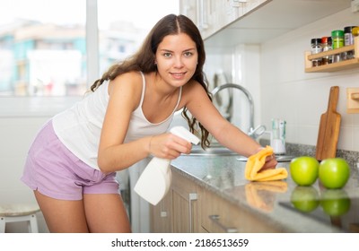 Young Positive European Woman Cleaning Kitchen Counter With Spray Bottle And Rag At Home