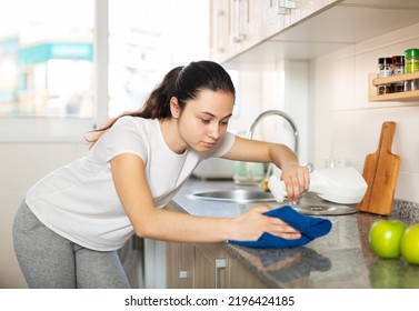 Young Positive European Woman Cleaning Kitchen Counter With Spray Bottle And Rag At Home