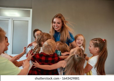 Young positive female dance teacher hugging happy children and smiling while standing in studio. Relationship between teacher and kids. Choreography class. Dance school