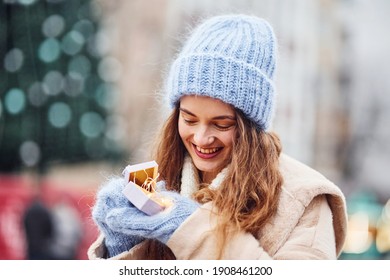 Young positive girl holds little gift box in hands outdoors in the city.