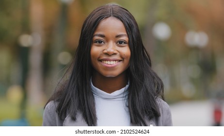 Young positive girl turns looking at camera businesswoman smiling with white teeth attractive happy african american woman outdoors close up adult pensive millennial lady in park portrait female face