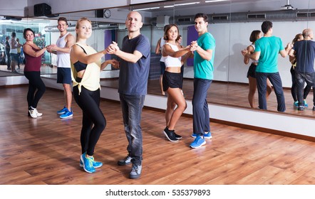 Young Positive Girls And Men Learning Salsa At Dance Class. Focus On Left Man