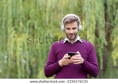 young positive man listen music in headphones and chating on phone outdoor