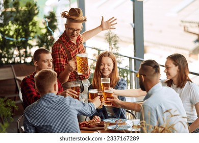 Young positive people, friends meeting st pub, cheerfully talking, drinking beer. Having food relaxed time together. Concept of oktoberfest, traditional taste, friendship, leisure time, enjoyment - Powered by Shutterstock