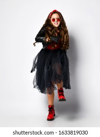 Young positive plus size girl model in bright rock style clothing, red boots and square glasses dancing over white background. Trendy youth casual fashion concept