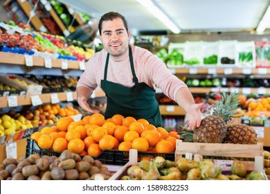 Young  positive smiling man in apron selling fresh oranges and fruits on the supermarket - Shutterstock ID 1589832253
